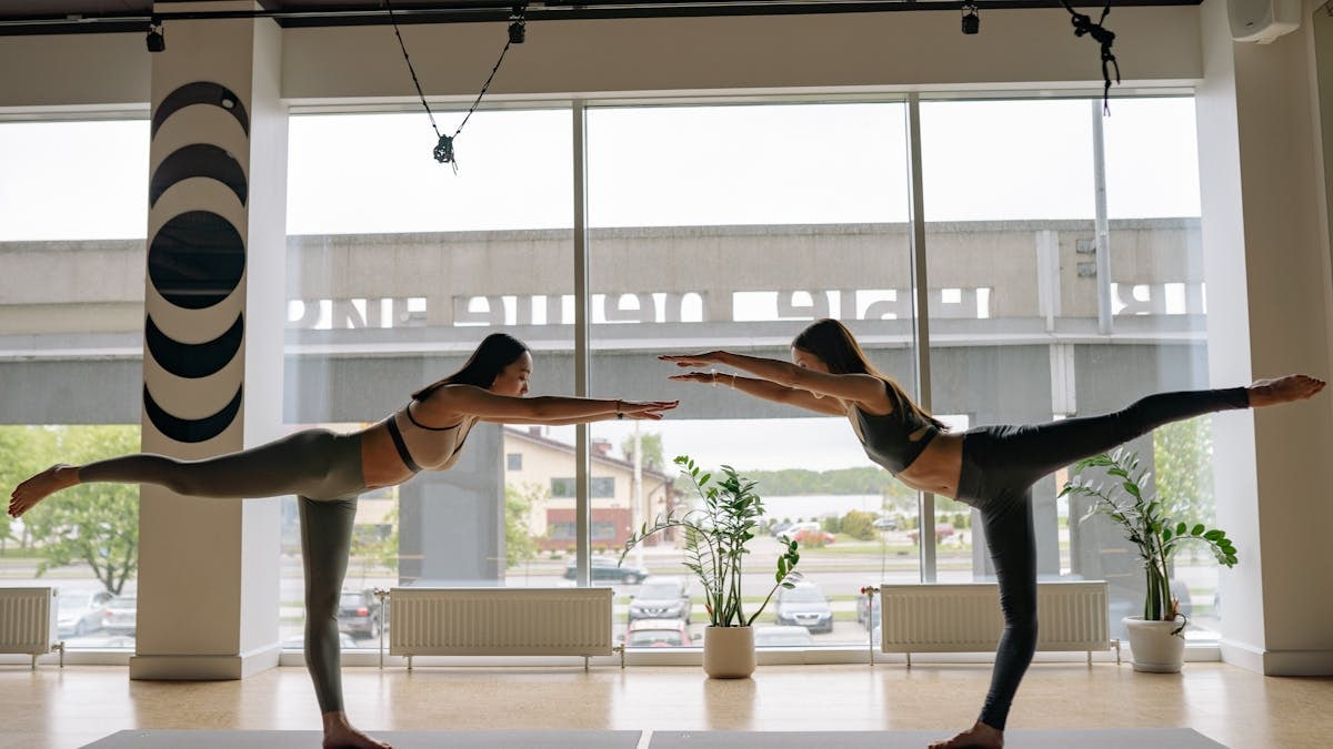Two women performing yoga poses in a contemporary indoor studio.