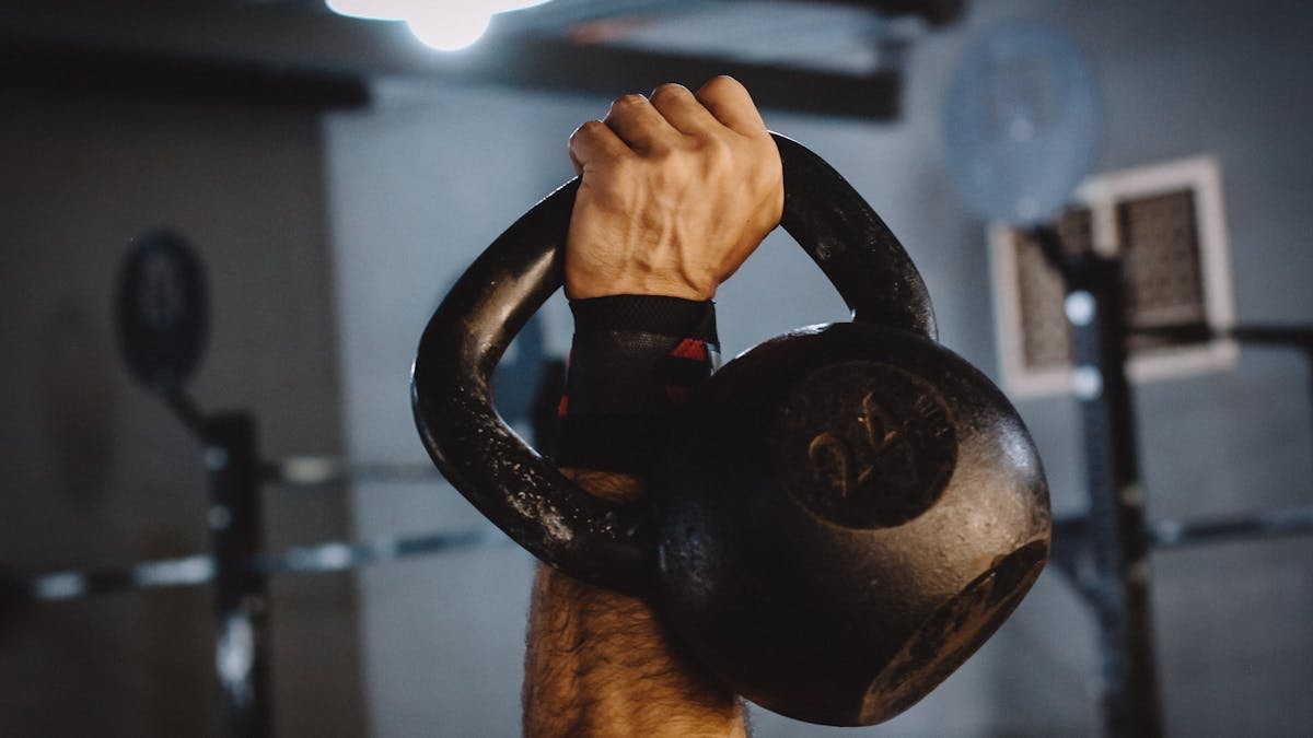 Focused shot of a person's hand lifting a kettlebell inside a gym, symbolizing strength and exercise.